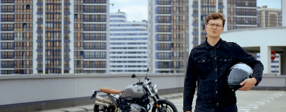 Un homme se tient devant une moto, sur un parking avec son casque dans la main